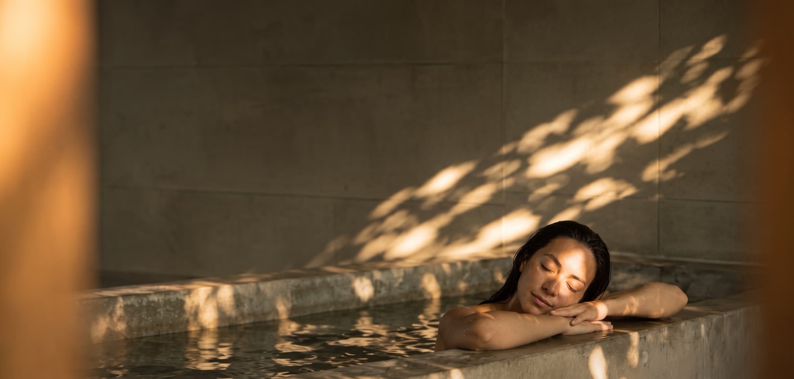 Woman resting at the edge of a warm stone onsen at golden hour